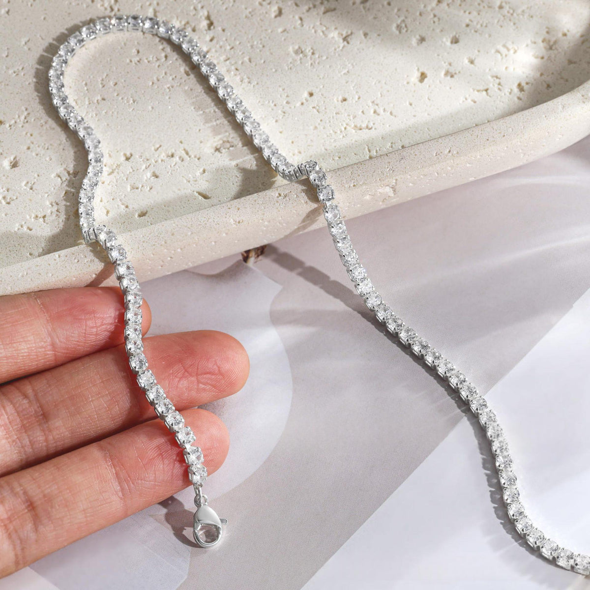 Collier tennis zircons argenté tenu à la main sur fond clair